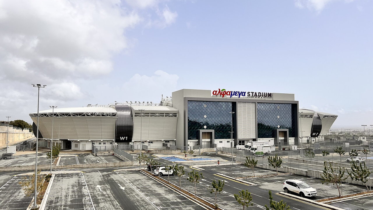 Alphamega Stadium in Paphos — Aussenansicht der grauen Stadionfassade mit dem Schriftzug des Namensgebers, davor der leere Vorplatz