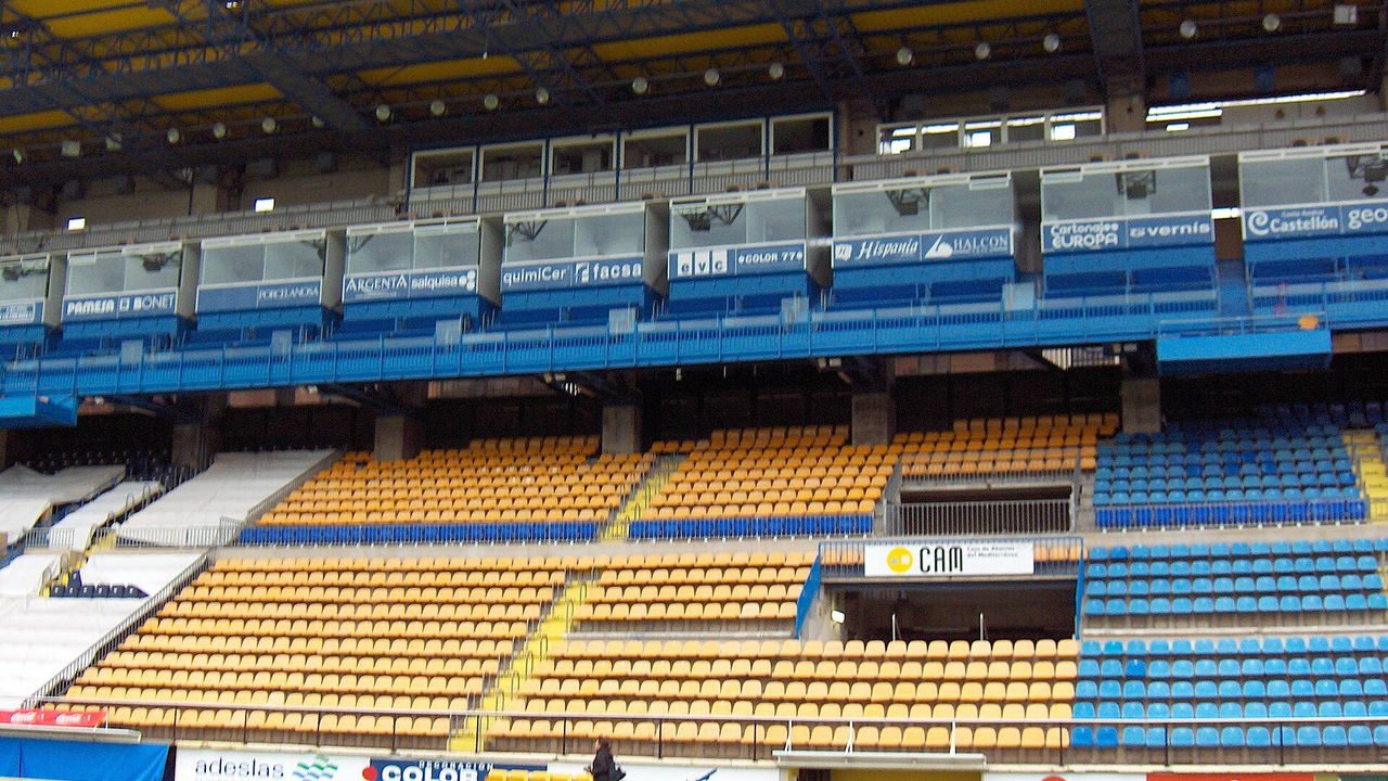 Estadio de la Cerámica in Villarreal — Tribüne mit gelben und blauen Sitzschalen, davor der Rasen und die Bandenwerbung