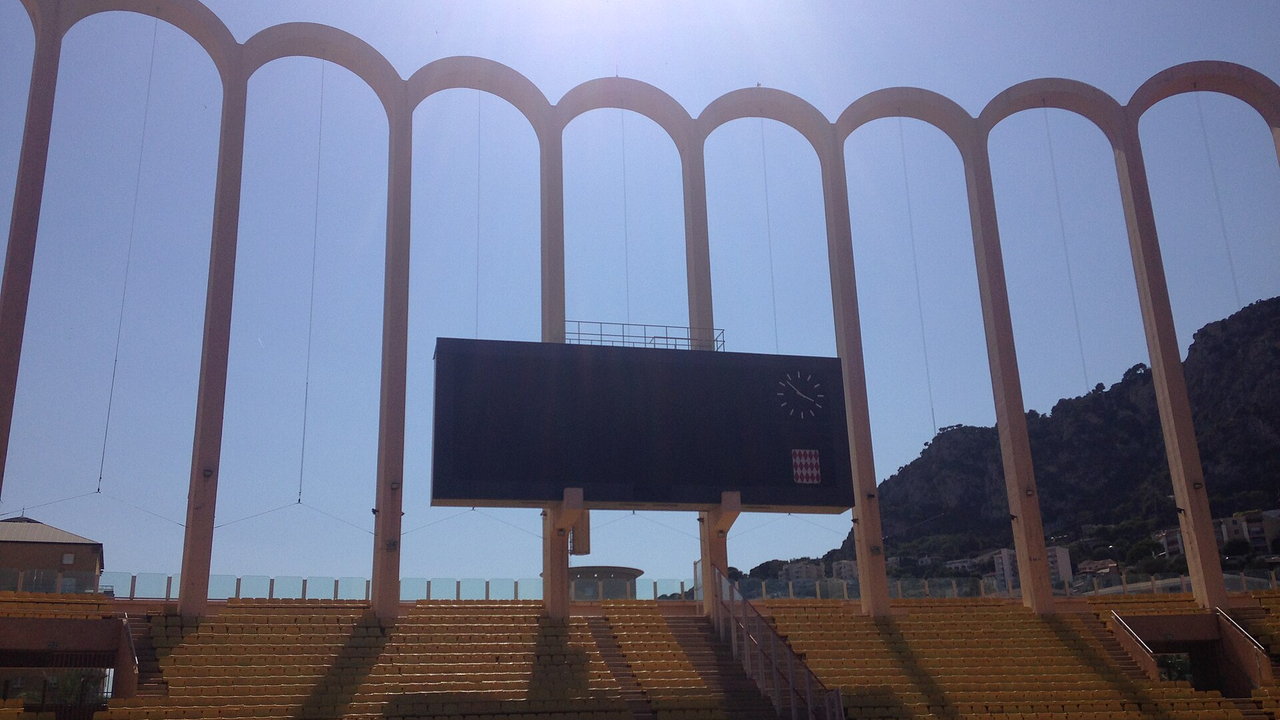 Stade Louis II in Monaco — Blick auf die Bogenreihe der Tribüne mit der Anzeigetafel, dahinter der Fels